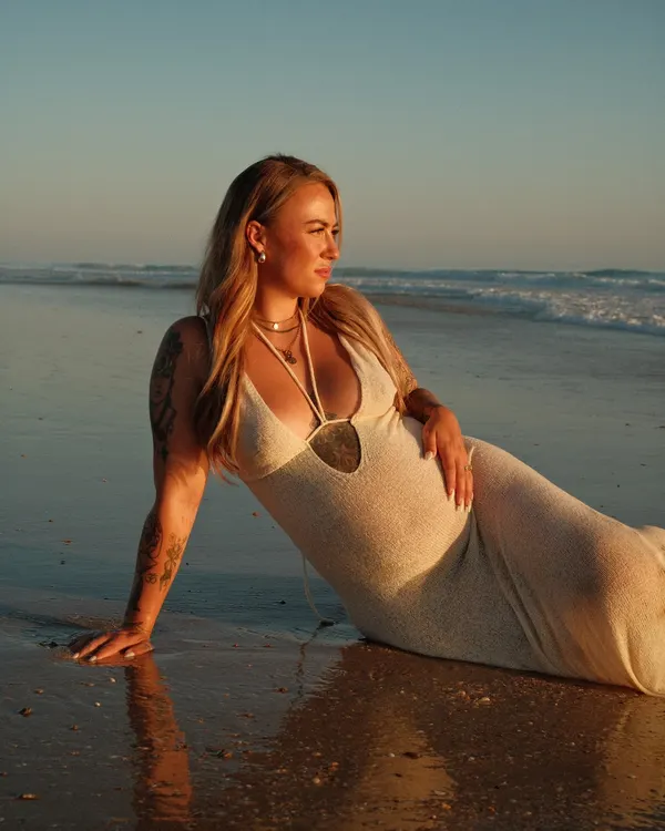 Pregnant woman lying at the water's edge at sunset